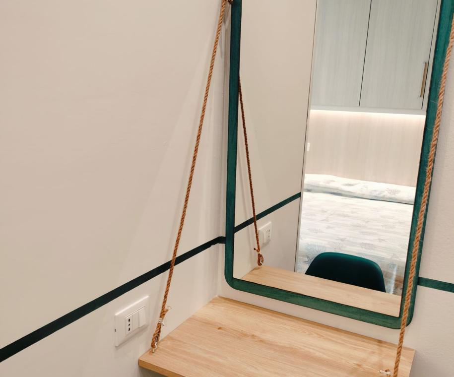 Specchio con corda, mensola in legno e sedia verde.