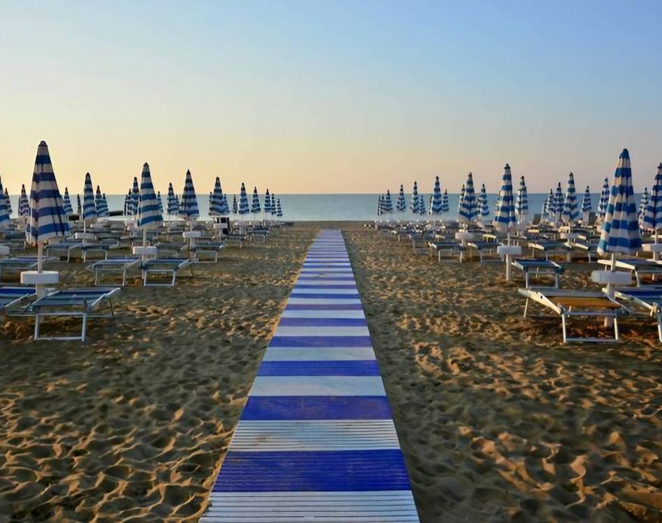 Beach with blue umbrellas and walkway at sunset.